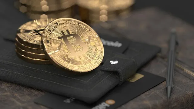 Gold-coloured Bitcoin tokens resting on a black wallet, with payment cards underneath.